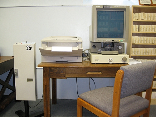 gray fabric and wood chair and brown wooden desk holding electronic machines for viewing and printing microform materials.