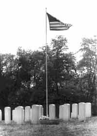 an American flag waves atop a flagpole surrounded by a grouping of identical white stone military veterans grave markers.