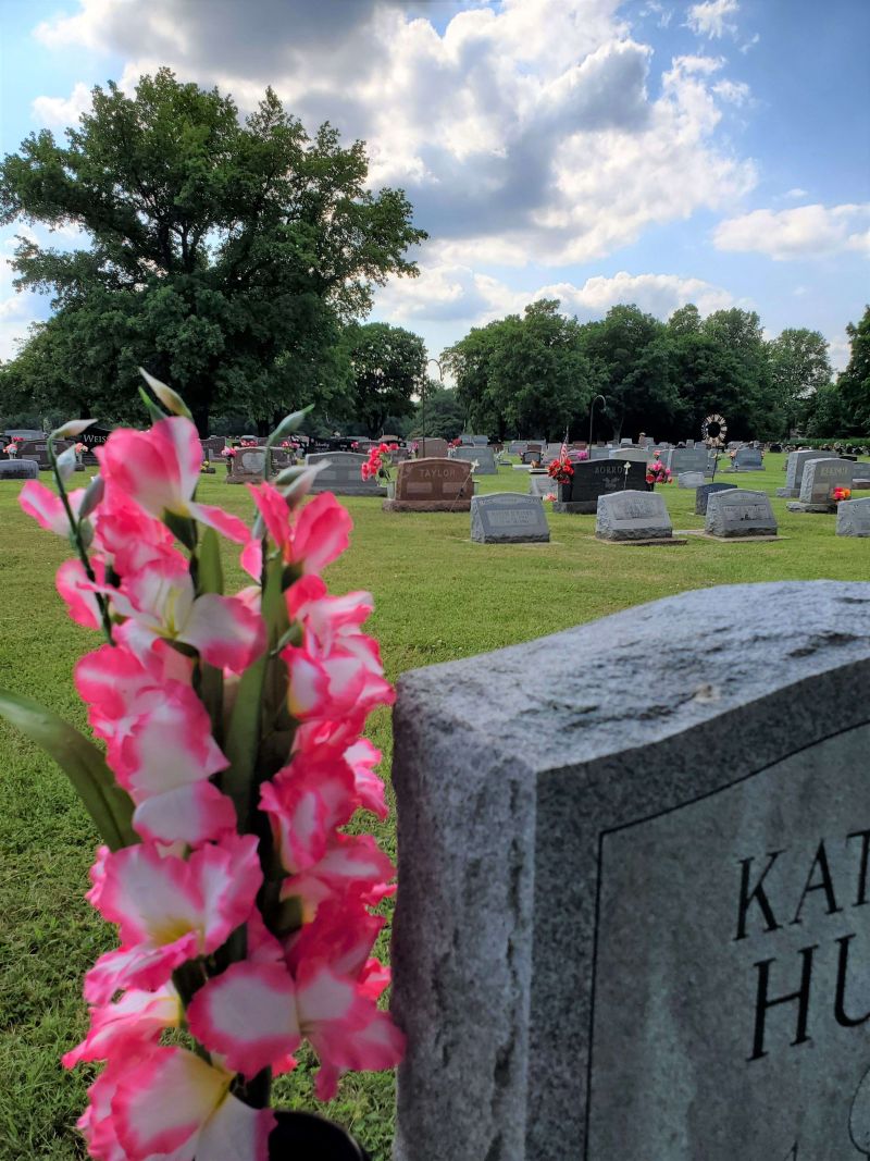 pink and white flowers in front of modern gray and brown tombstones in grassy expanse