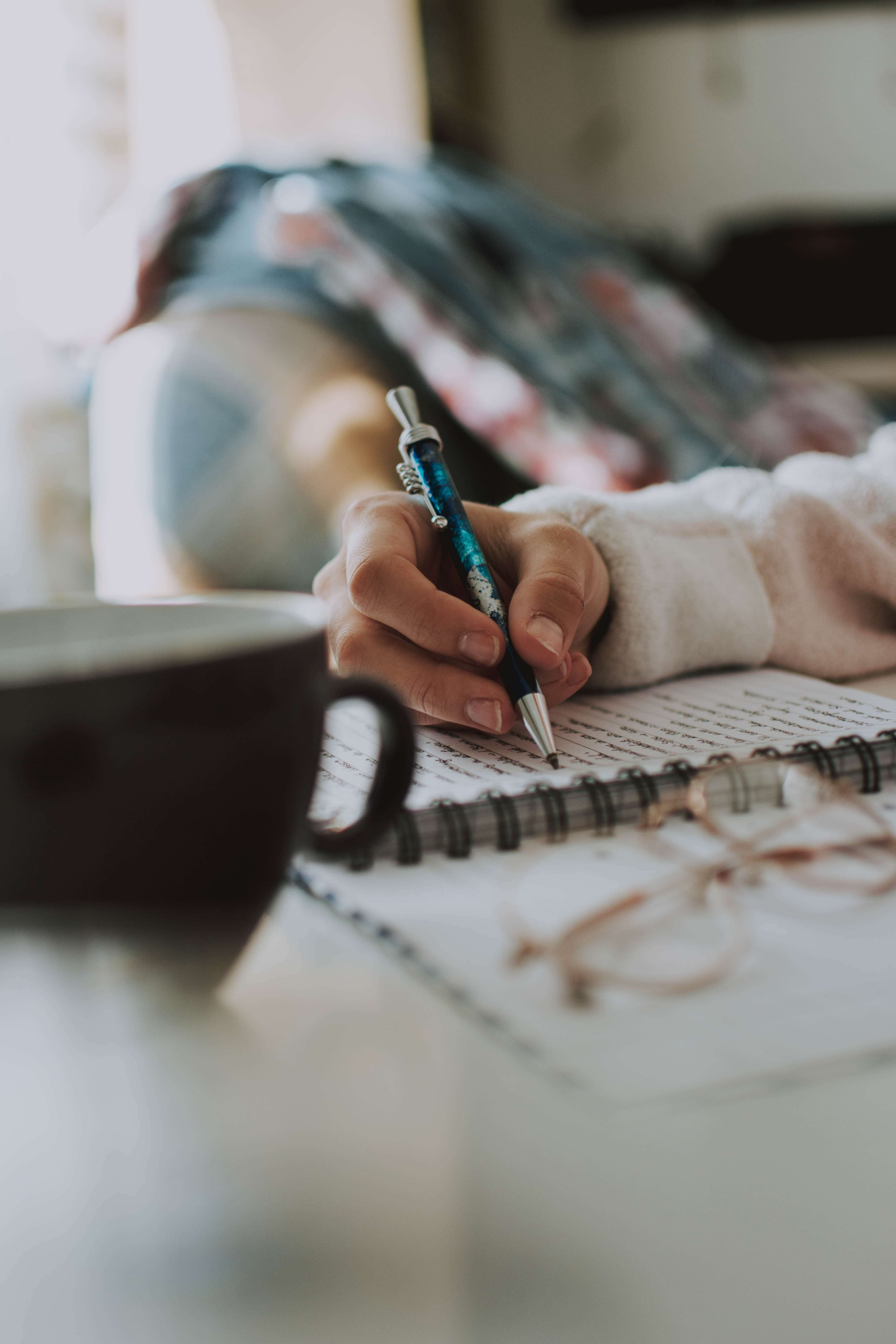 human hand holds ball point pen and writes in a spiral bound notebook